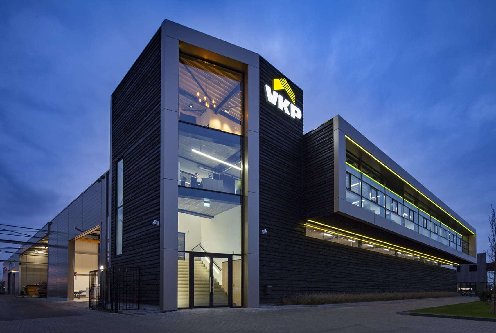 Het verlichte kantoor van VKP in de avond, met werkplekken van engineering en werkvoorbereiding boven de productiehal.