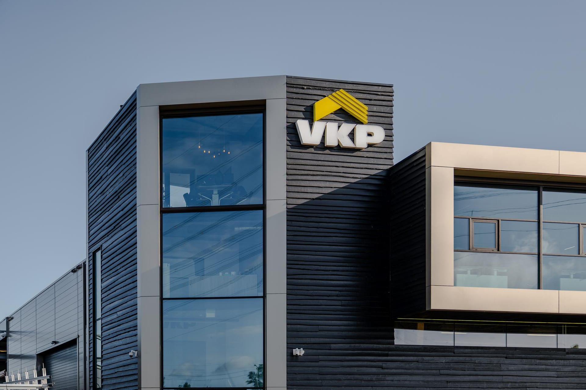 Het hoofdkantoor van VKP in Kapelle met zwarte houten gevelbekleding en het VKP-logo, gezien bij avondlicht.