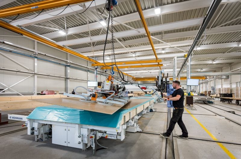 Houtskeletbouwelement op de productietafel in de hal, met een medewerker aan de besturing.
